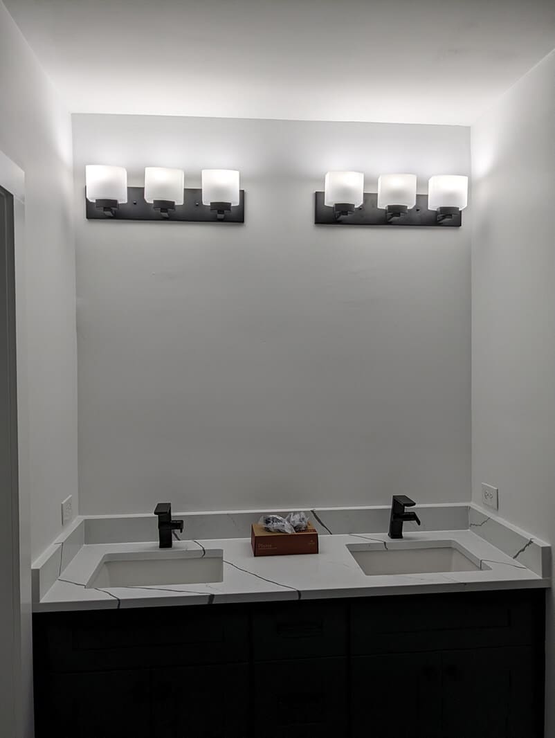 A bathroom with two sinks and lights above the sink.