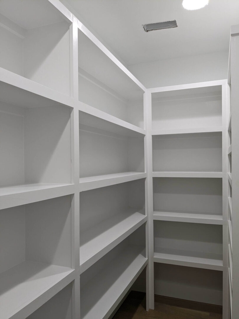 A white pantry with many shelves and no doors.