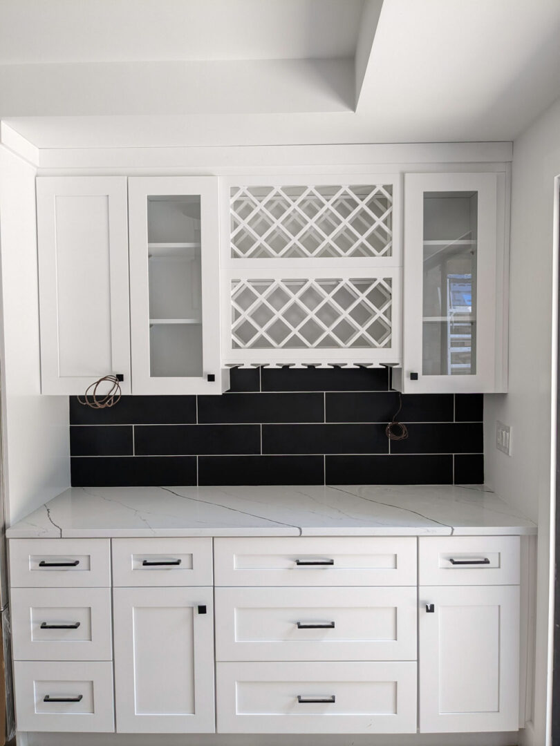 A kitchen with white cabinets and black tile backsplash.