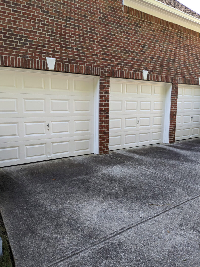 Three white garage doors in a brick wall.