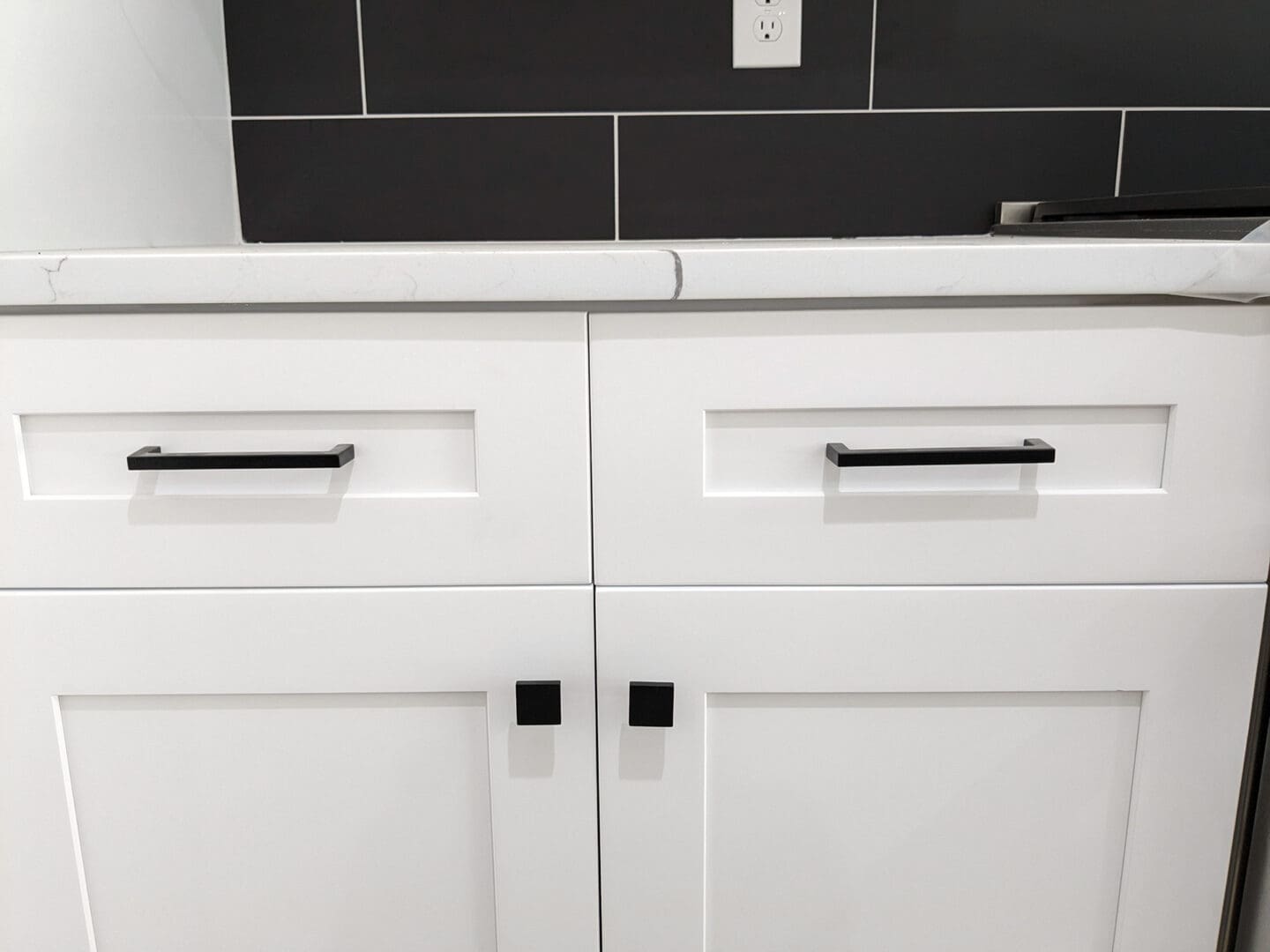 A white cabinet with black handles and knobs.