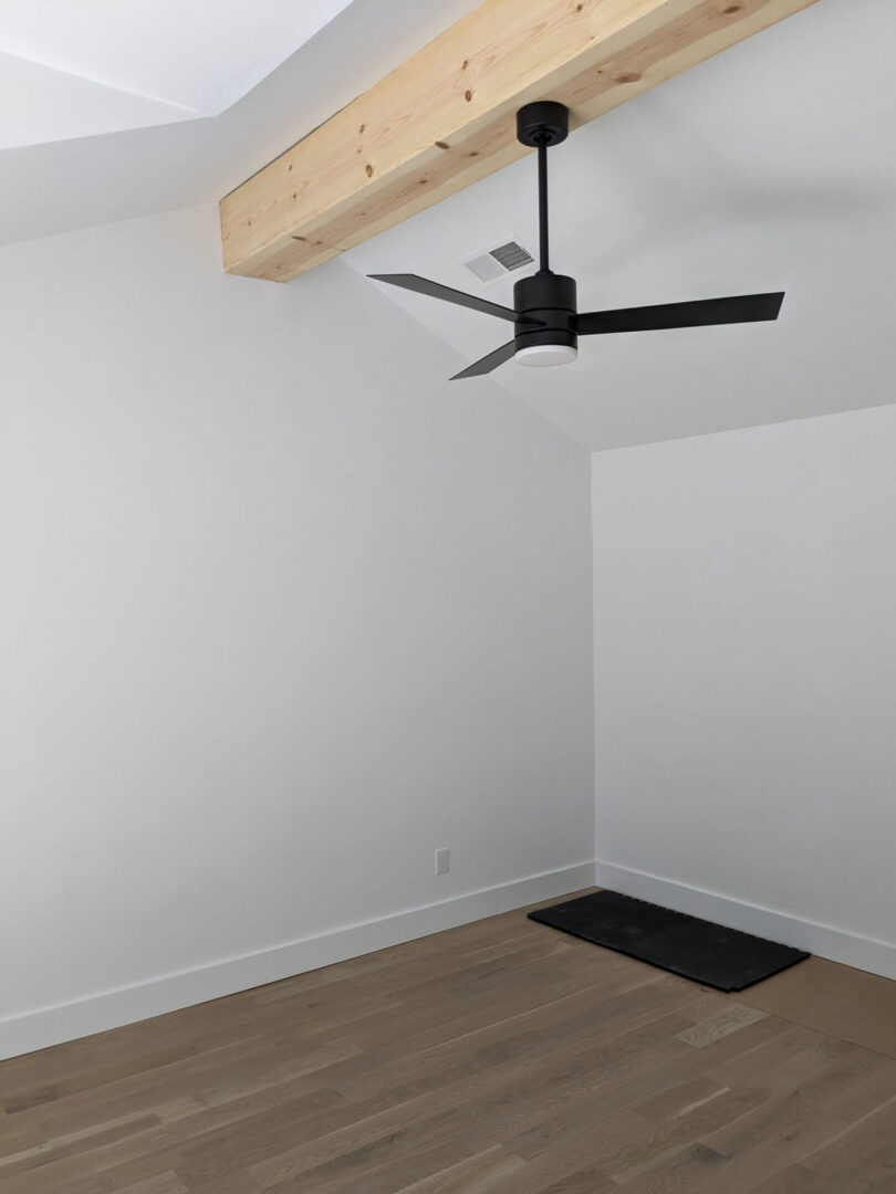 A room with a ceiling fan and wooden beams.